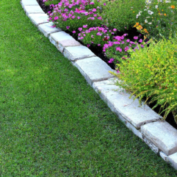 description: an anonymous image showcasing a neatly manicured lawn with defined edges, bordered by colorful flowers and shrubs. the edges are lined with stone blocks, creating a clean and polished look to the landscape.