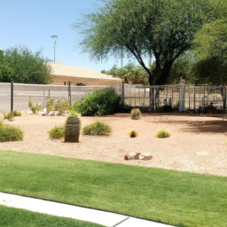 A picture of a yard with green grass, plants, trees, and a fence, all surrounded by a desert landscape.