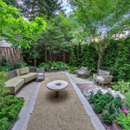 Description: An anonymous image of a beautiful patio with a seating area, surrounded by greenery and decorative elements. The seating area consists of a table and chairs with cushions, and there are decorative planters and a sculpture nearby. The patio is bordered by a pathway made of natural stone, and there are plants and trees surrounding the area.